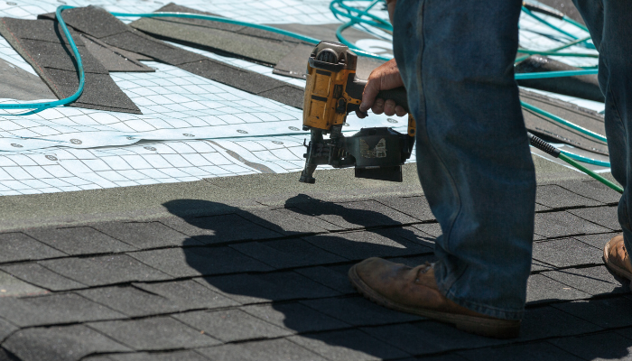 Worker using a nail gun to attach tiles on a roof